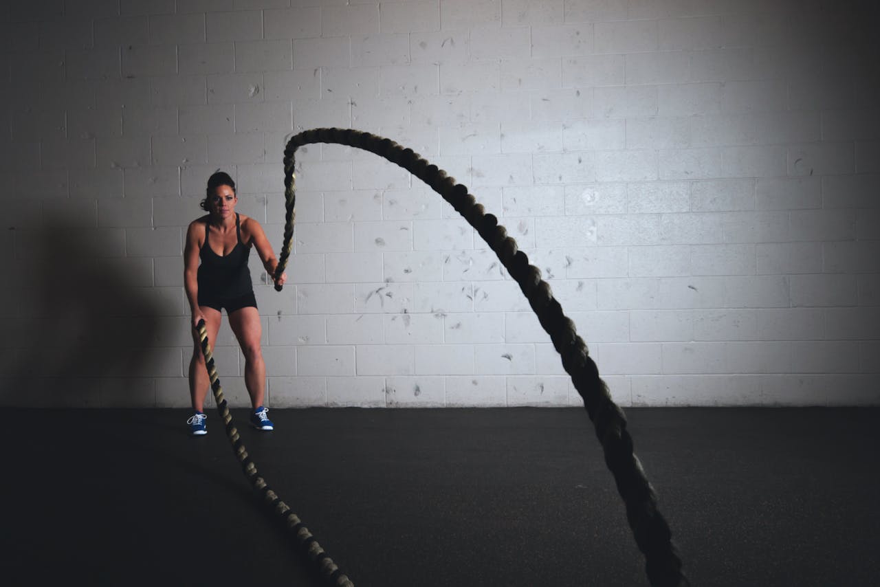 services-02 A focused woman performs a dynamic battle rope exercise in a gym setting, demonstrating strength and fitness.